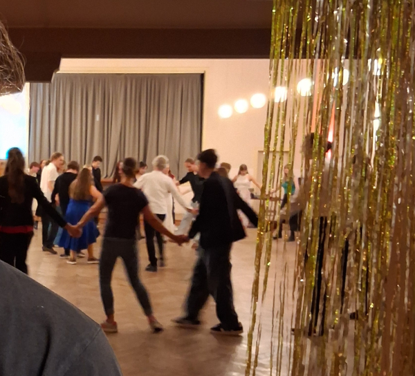 Junge Menschen tanzen hinter einem gold-glitzernden Vorhang im Kreis